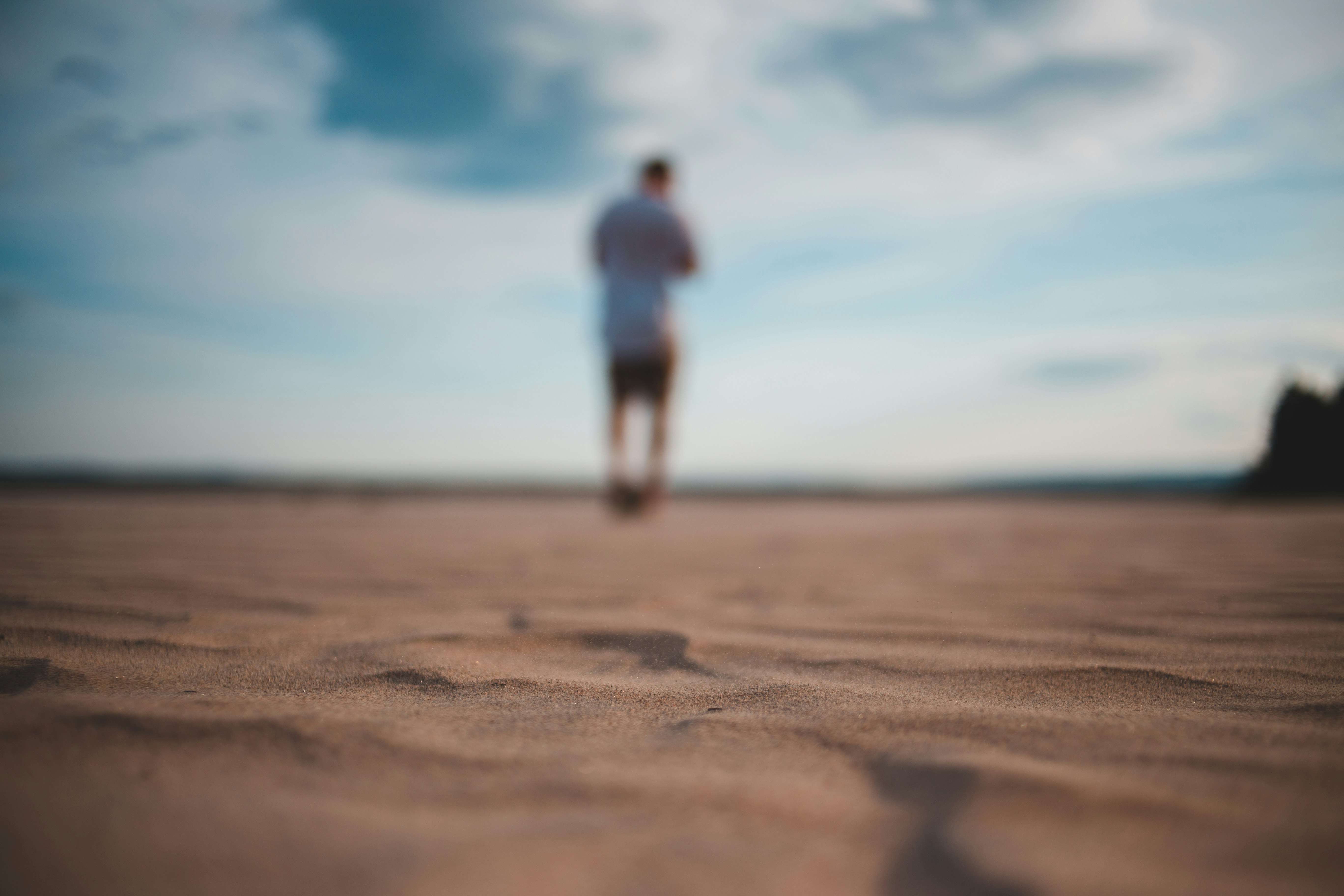 man in white t-shirt and blue denim jeans walking on brown sand during daytime